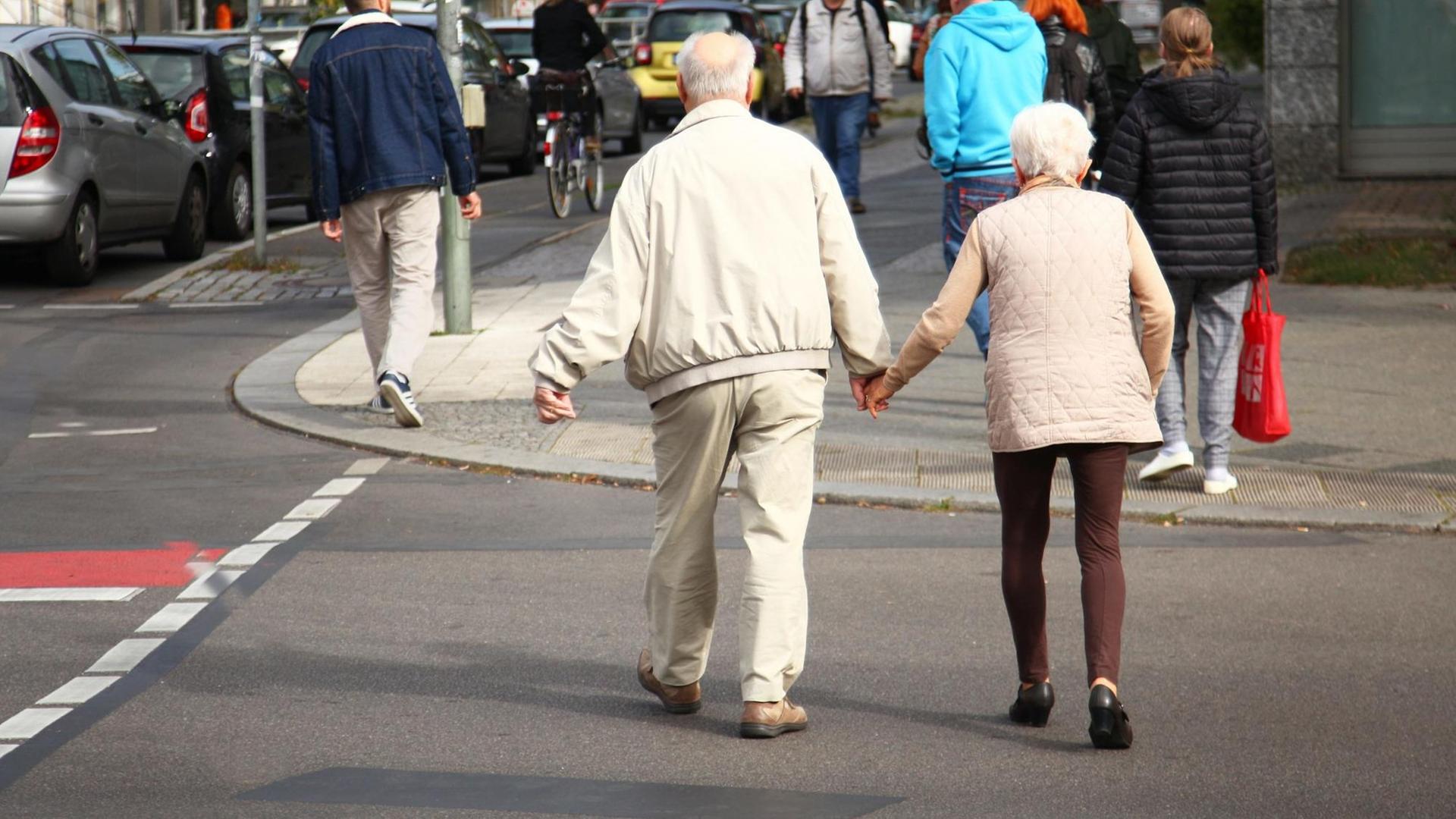 Ein Rentnerpaar überquert eine Straße.