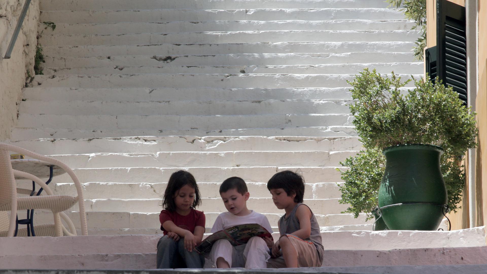 Nauplia, Griechenland: Drei Kinder sitzen mit einer Zeitschrift auf den Stufen einer großen Treppe.