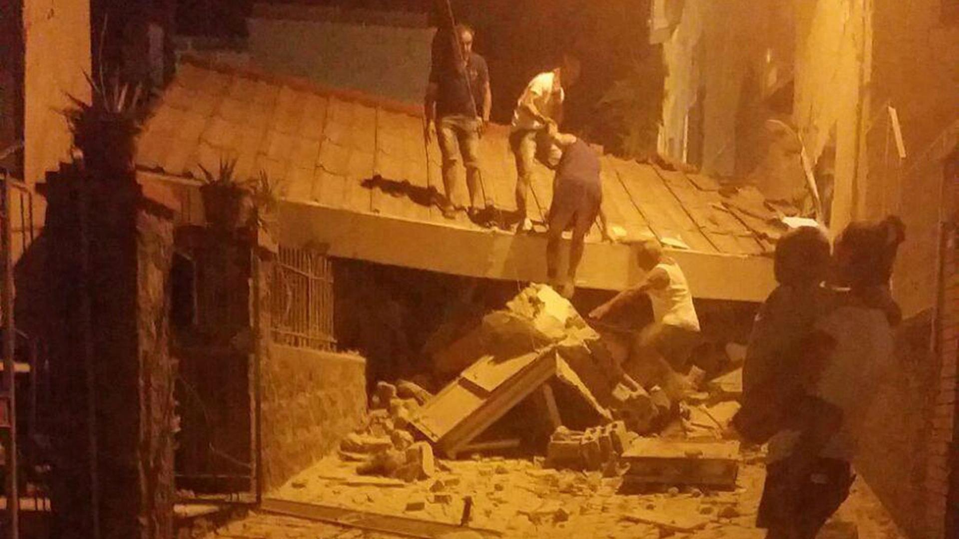 Menschen in der Dunkelheit auf einem abgesackten Dach nach dem Erdbeben in Ischia; am Boden Trümmer.