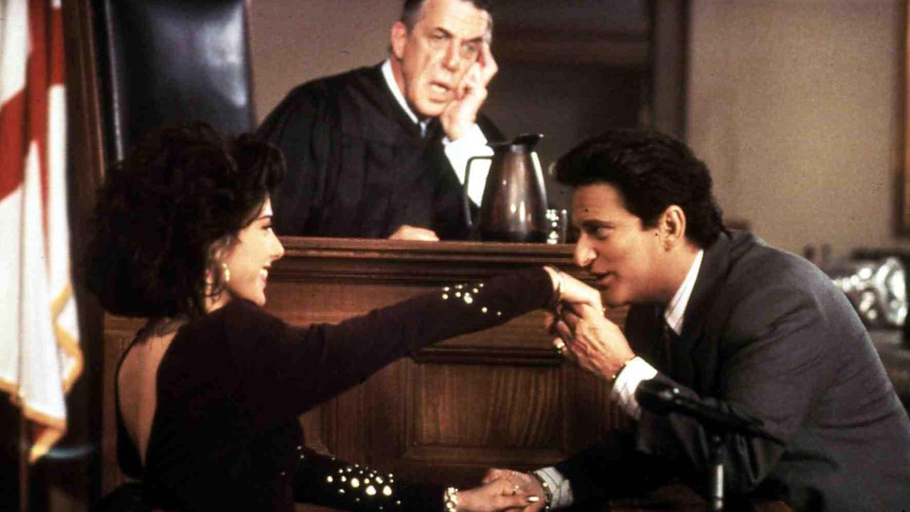 Szene aus "Mein Cousin Winnie" im Gericht: Joe Pesci küsst Marisa Tomei die Hand, während sie im Zeugenstand ist, im Hintergrund Fred Gwynne auf dem Richterstuhl.