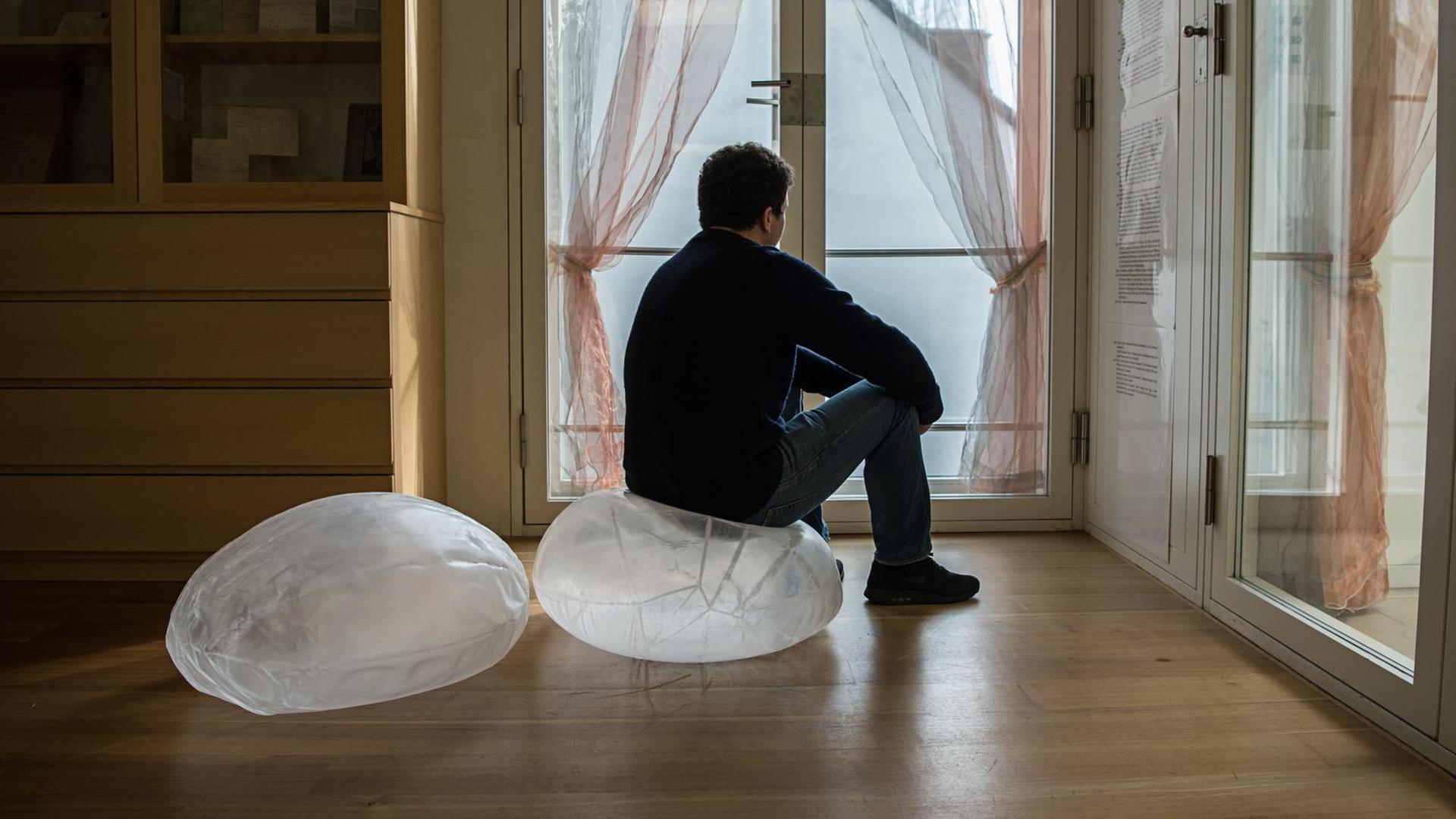 Ein Mann sitzt in einem Raum mit Holzfußboden auf einem durchsichtigen Sitzsack.