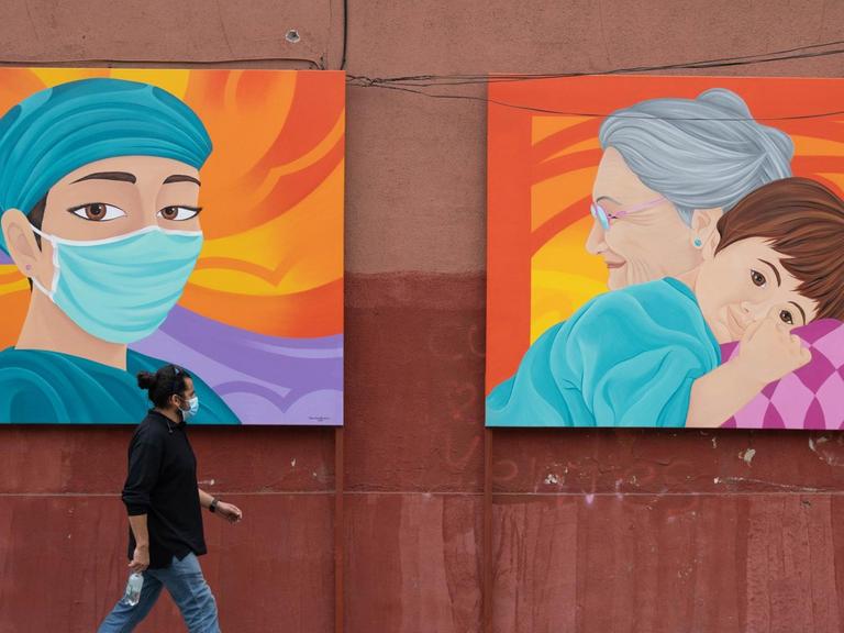 Ein Fußgänger mit Mund-Nasen-Bedeckung geht in Santiago de Chile an einer Mauer entlang mit zwei Malereien, die zu Ehren des Gesundheitspersonals angefertigt wurden.