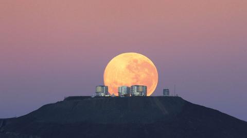 Orangefarbener Mond während seines Untergehens über einem Berg mit Himmelsbeobachtungsstation