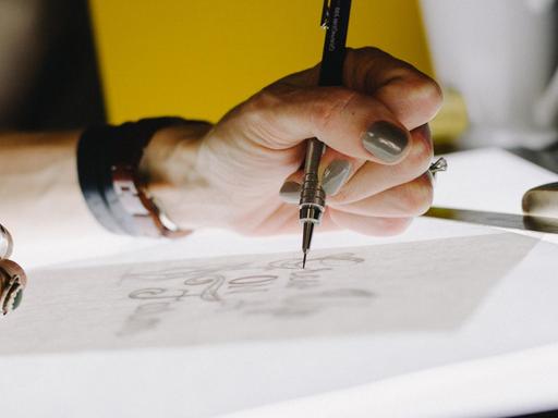 Eine Hand skizziert mit einem ganz feinen Stift etwas auf einem Papier.