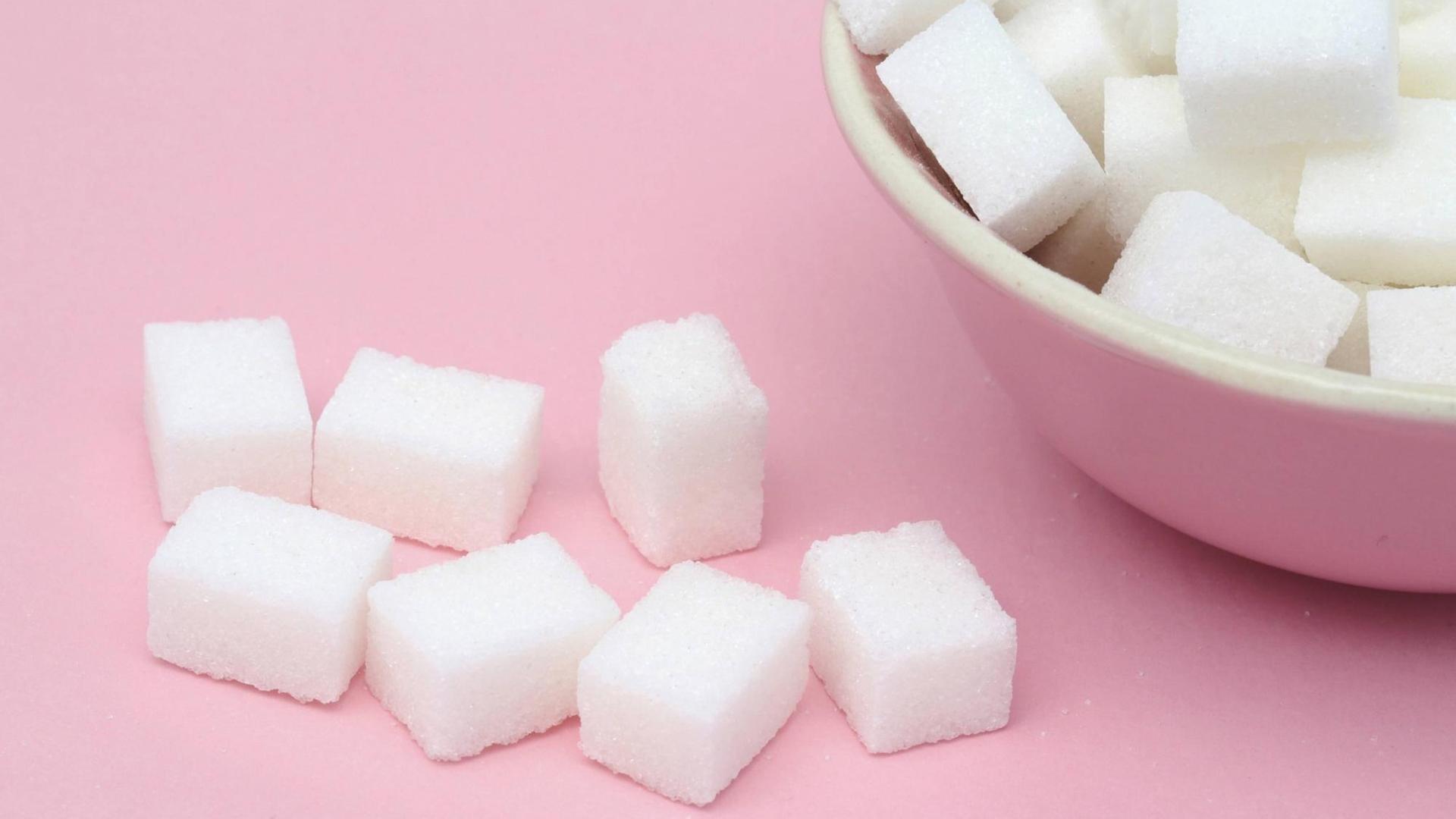 Mehrere Stücke Würfelzucker liegen auf dem Tisch und in einem Schälchen. Mehrere Stücke Würfelzucker liegen auf dem Tisch und in einem Schälchen.