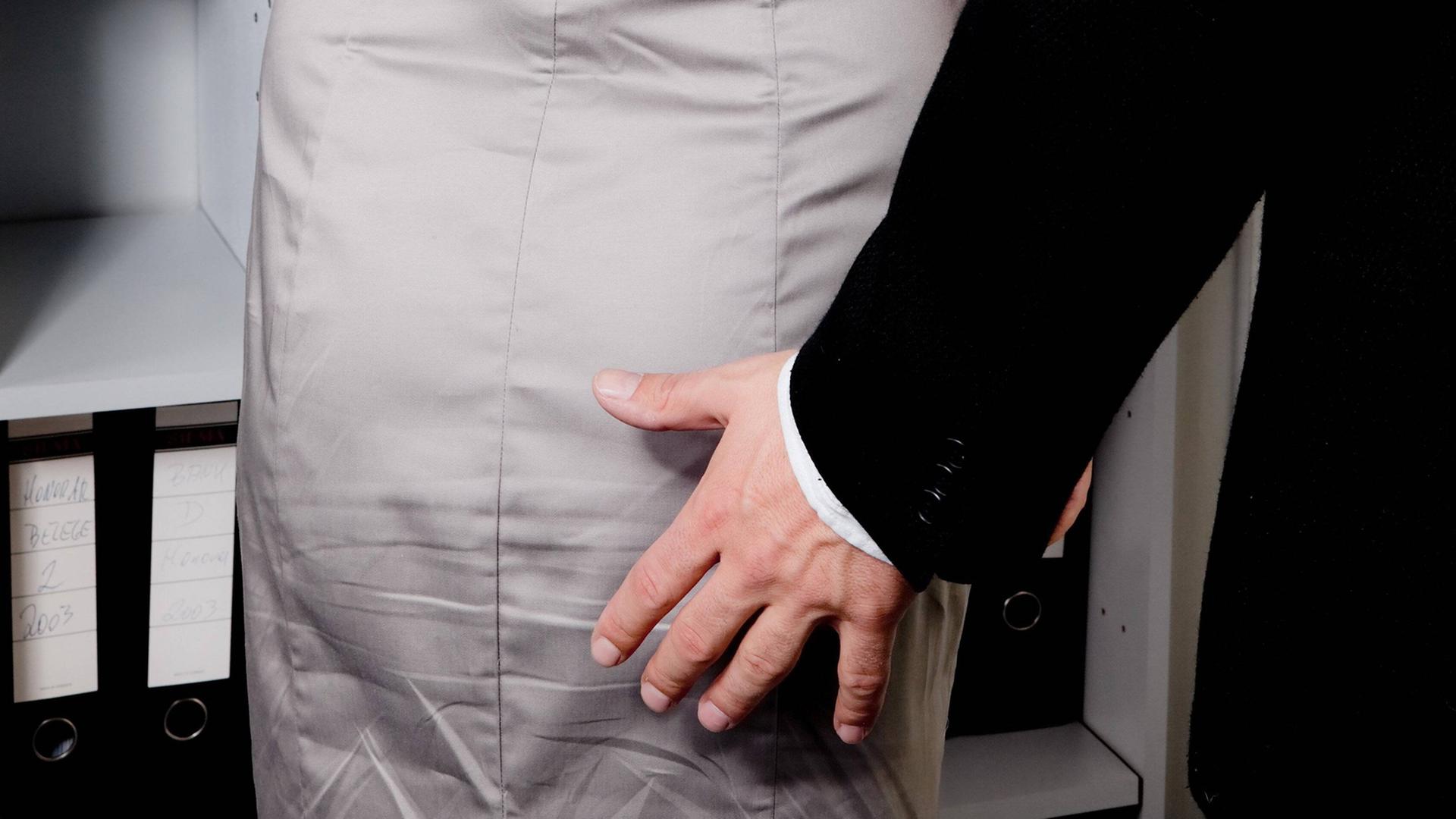 Eine männliche Hand bewegt sich zum Gesäß einer Frau in einem Büro. (Symbolbild)