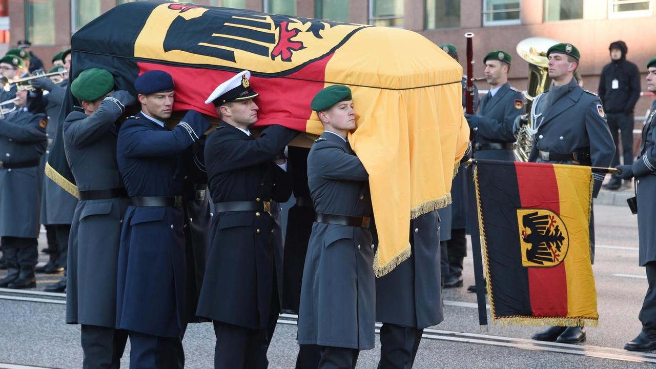 Mehrere Sarg-Träger tragen den Sarg von Helmut Schmidt. Der Sarg ist mit einer Deutschland-Flagge bedeckt.