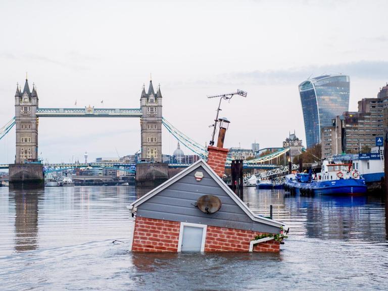 Ein nachgebildetes britisches Haus schwimmt, zur Hälfte im Wasser versunken, vor der Tower Bridge in der Themse. "Our house is flooding'" heisst die Kunstaktion der Umweltschutzgruppe Extinction Rebellion.