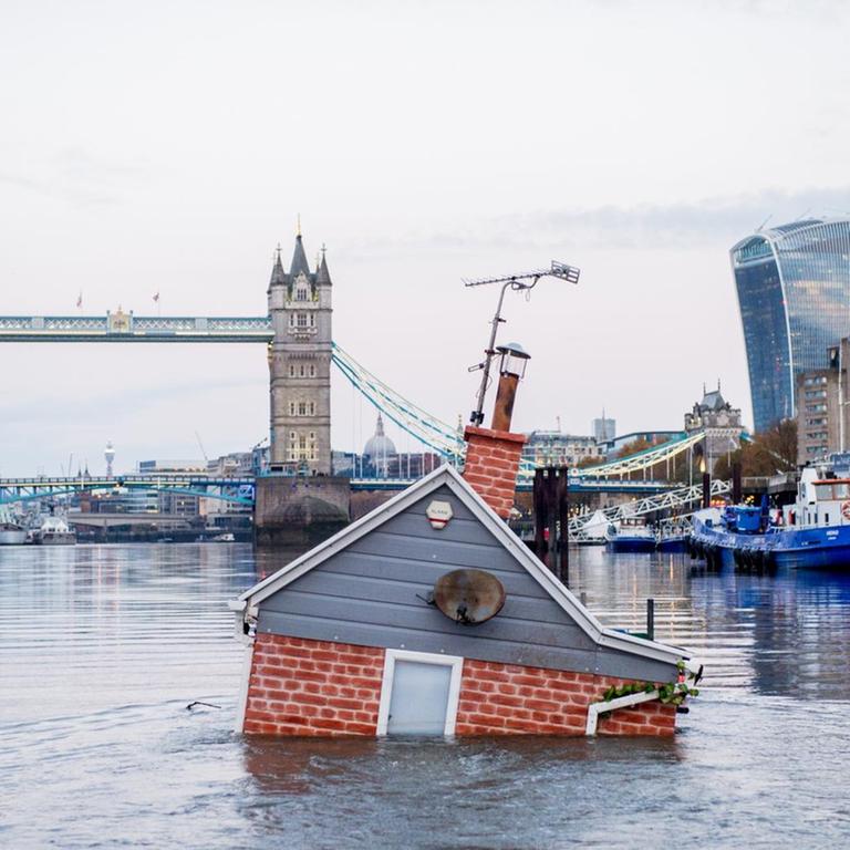 Ein nachgebildetes britisches Haus schwimmt, zur Hälfte im Wasser versunken, vor der Tower Bridge in der Themse. "Our house is flooding'" heisst die Kunstaktion der Umweltschutzgruppe Extinction Rebellion.