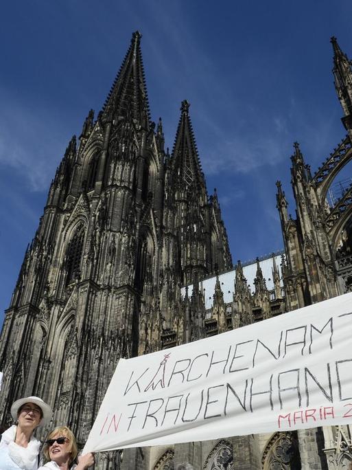 Demonstrantinnen der Bewegung Maria 2.0 stehen mit einem Transparent mit der Aufschrift "Kirchenamt in Frauenhand - Maria 2.0" vor dem Kölner Dom.