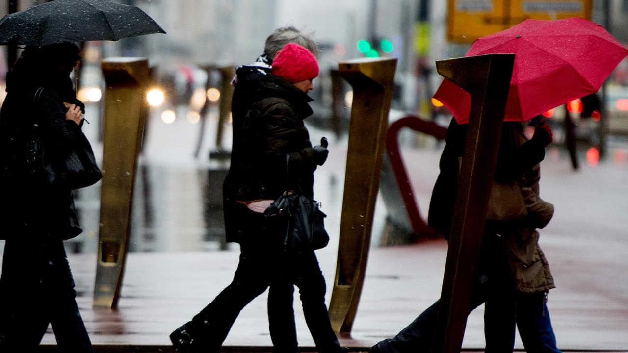 Passanten schützen sich am 10.12.2014 am Potsdamer Platz in Berlin mit Schirmen vor dem Regen.
