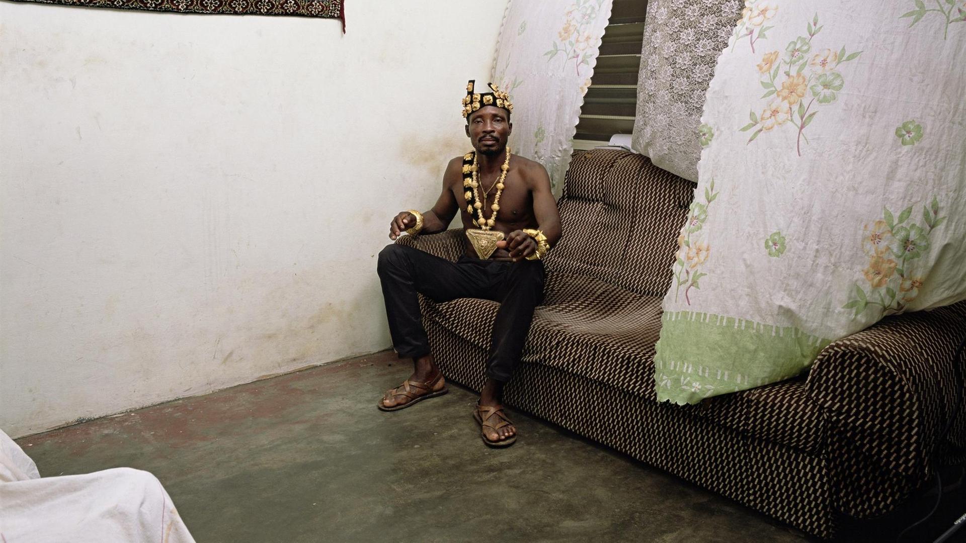 Deanna Lawson: Chief, 2019. Das Foto zeigt einen Mann mit Goldkrone und Goldkette auf einem alten Sofa sitzend.