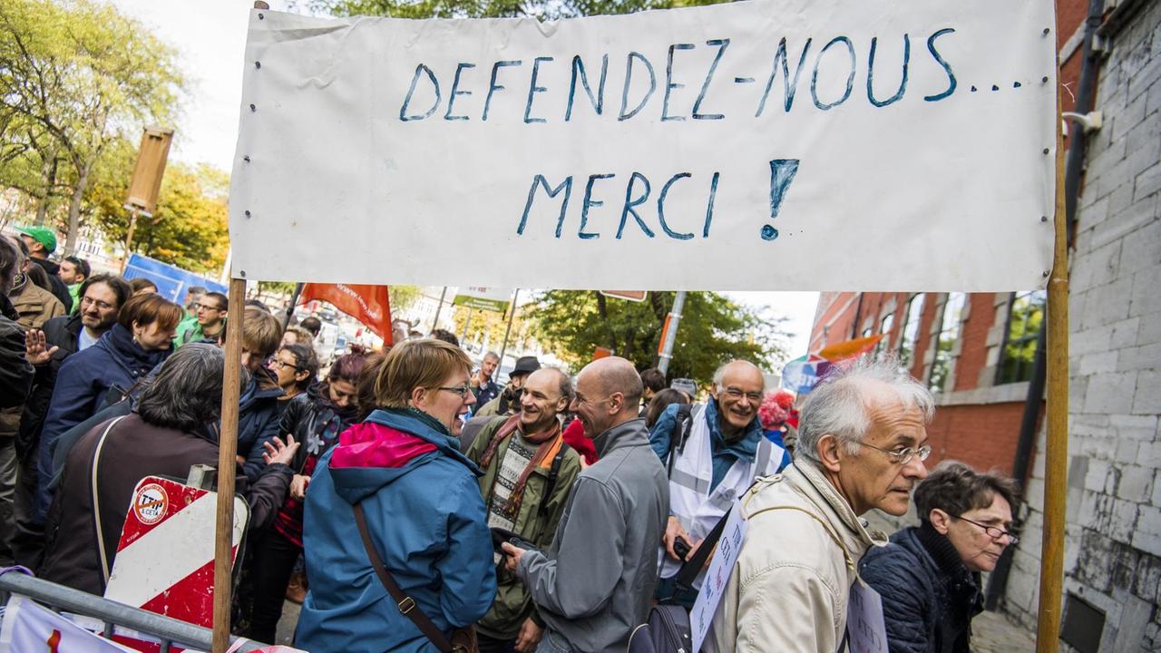 Das Bild zeigt viele Demonstranten sowie ein Transparent mit der Aufschrift "Defendez-Nous... Merci!"
