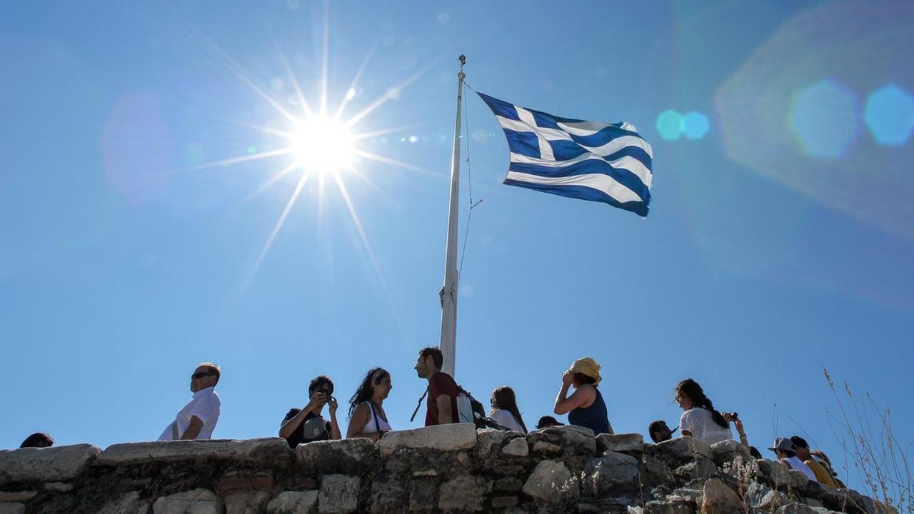 Die griechische Flagge ist hier auf der Akropolis zu sehen, darunter stehen Menschen