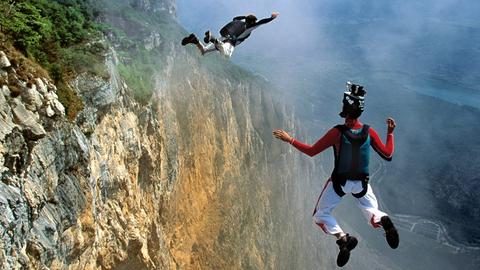 Zwei junge Männer springen als Basejumper von einem hohen Berg.