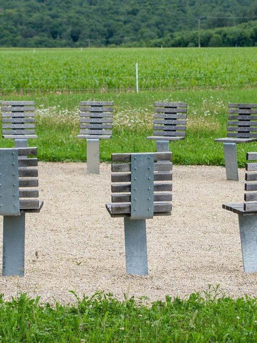 Vor einer grünen Landschaft sind im Freien in Rund Stühle aufgestellt, die fest im Boden verankert sind.