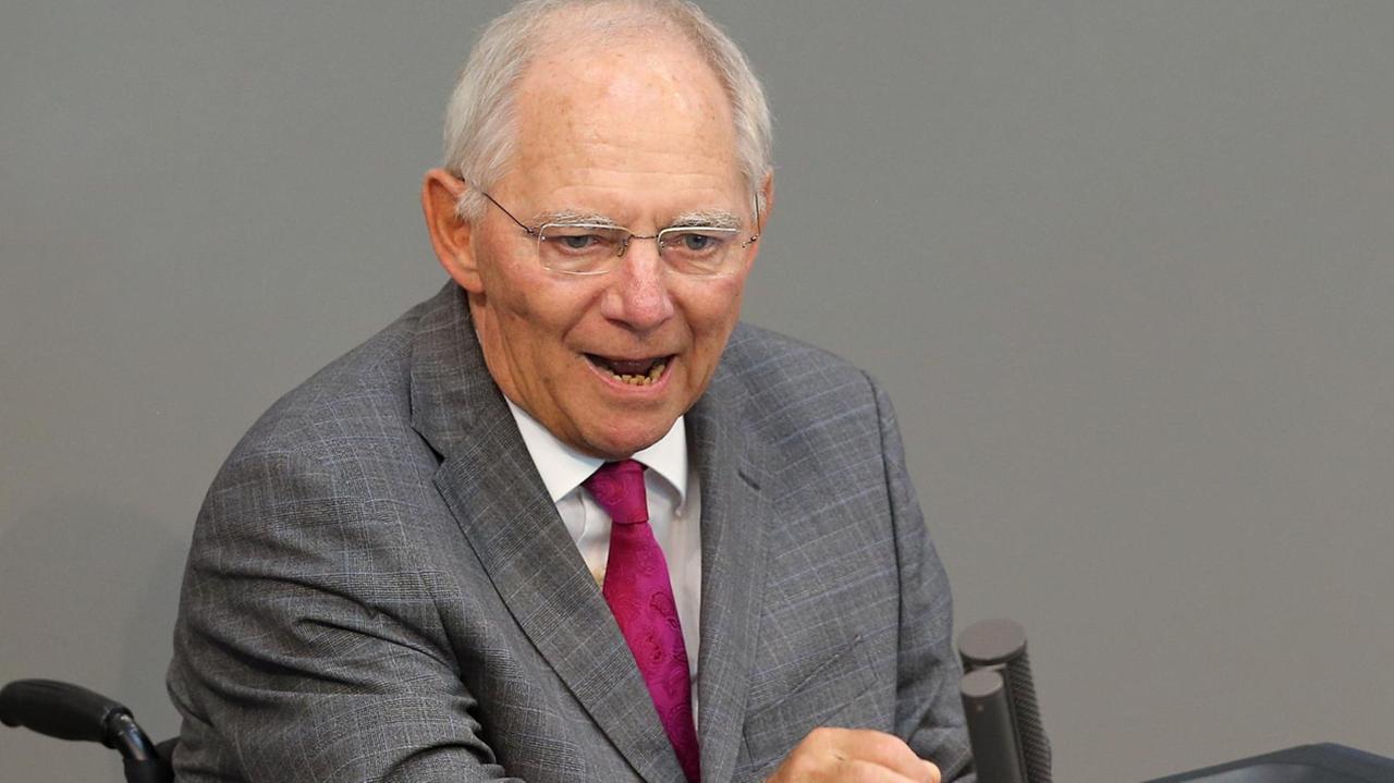 Schäuble sitzt im Rollstuhl am Rednerpult und spricht. Er gestikuliert dabei mit der rechten Hand.