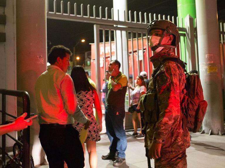 Ein Soldat mit Atemmaske beäugt in Lima Menschen, die einen Supermarkt betreten wollen. In Peru wurde wegen der Corona-Pandemie der Katastrophenfall ausgerufen.