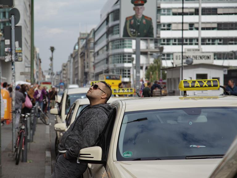 Ein Taxifahrer hält einen Moment inne und lehnt sich gegen sein Taxi am Checkpoint Charlie in Berlin.