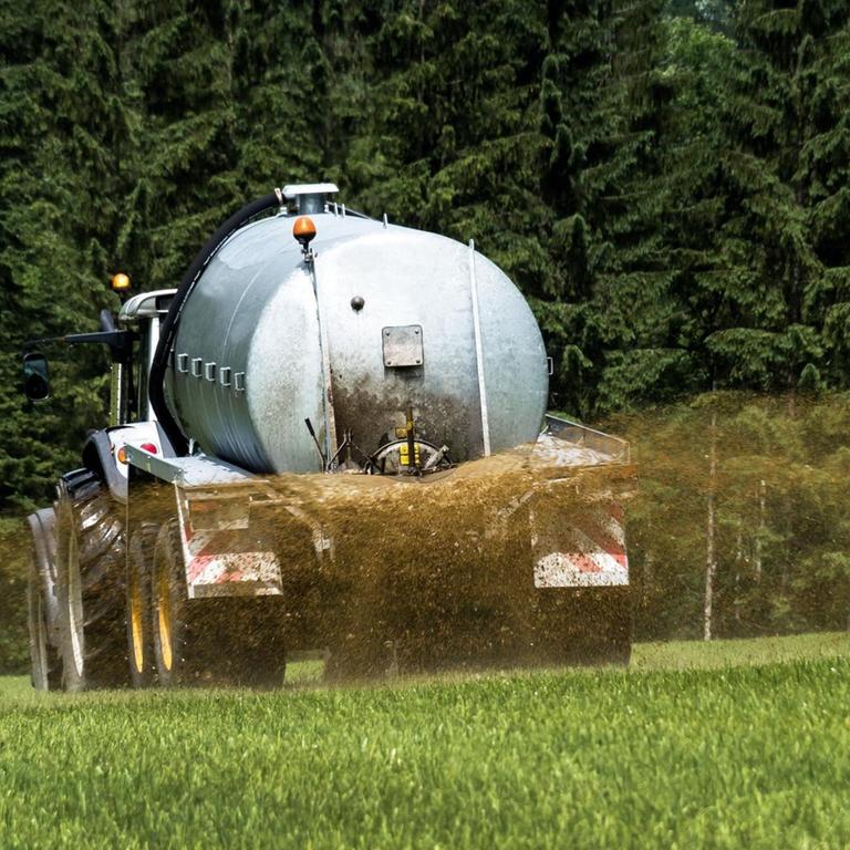 Ein Bauer bringt mit einem Traktor Gülle auf ein Feld.