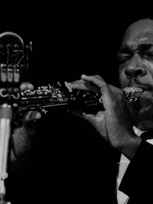 Ein Schwarz-Weiß-Portrait von John Coltrane am Saxophon - sein Instrument bildet mit dem Mikrofon ein Kreuz.