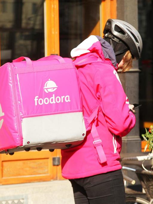 Eine Fahrerin von Foodora steht in Berlin im Bezirk Mitte an ihrem Fahrrad.