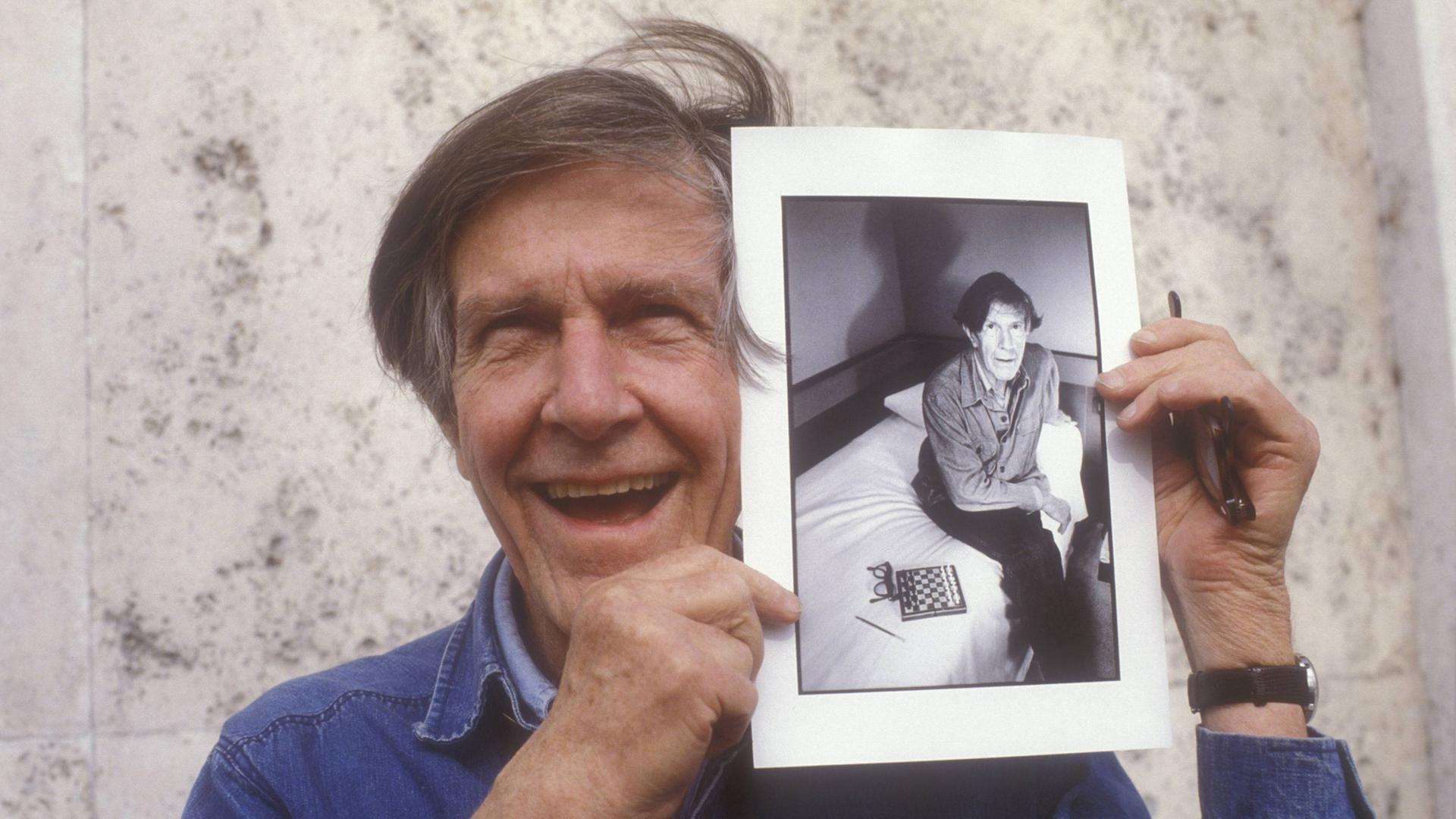 Der US-amerikanische Komponist John Cage (1912 – 1992) zeigt ein Foto von sich aus den frühen 80er-Jahren