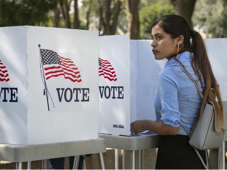 Eine junge Wählerin in den USA steht zwischen "Vote" Schildern.
