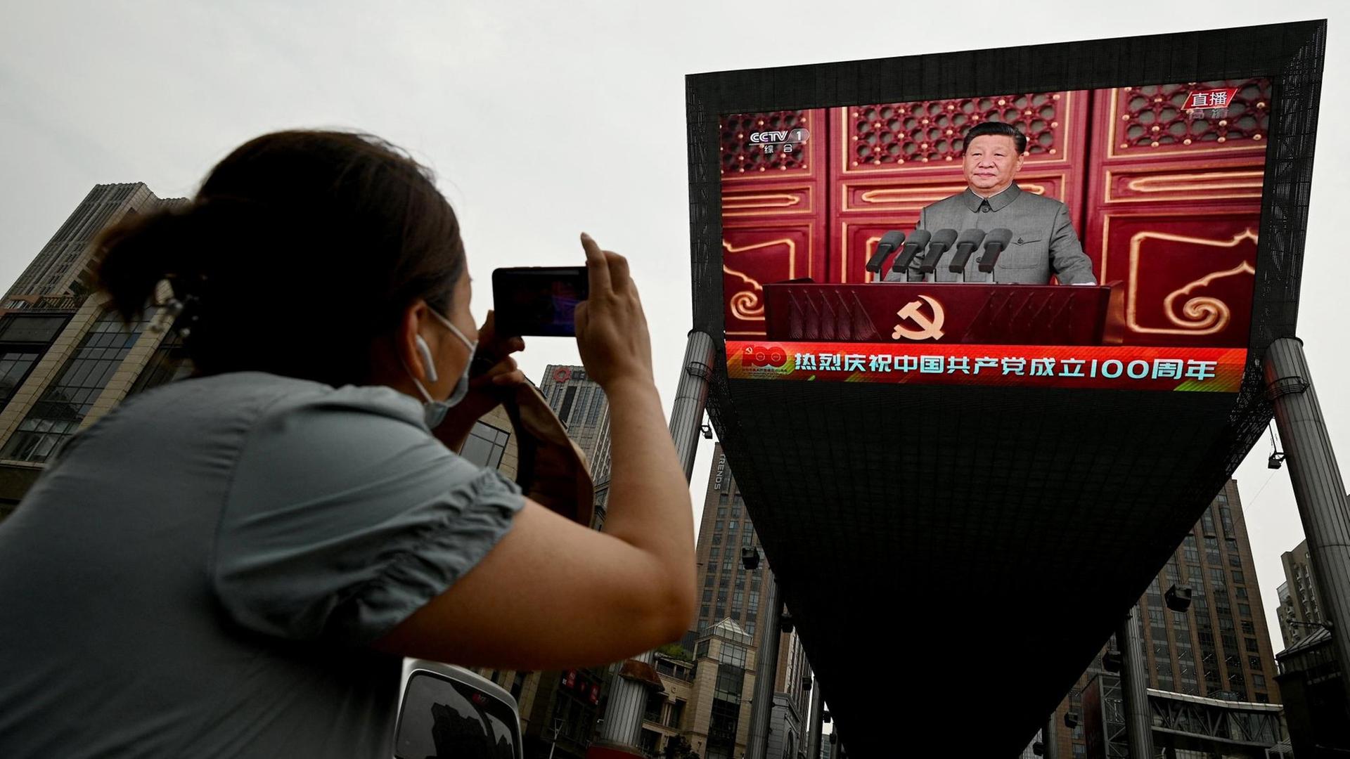 Eine Frau fotografiert eine Rede vom chinesischen Präsidenten Xi Jinping auf einem grossen Bildschirm auf der Strasse in Beijing während der 100-Jahres-Feier der kommunistischen Partei. China, 1.Juli 2021.