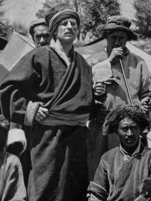Schwarz-weiß-Aufnahme von einer Gruppe Tibetaner, in deren Mitte Sven Hedin in deren traditioneller Kleidung steht.