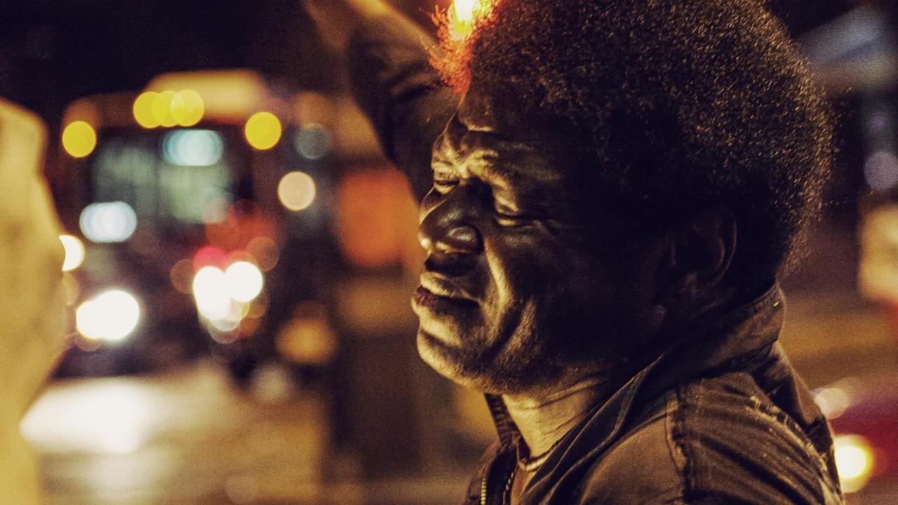 Charles Bradley mit geschlossenen Augen in einer nächtlich-urban erleuchteten, unscharfen Umgebung.