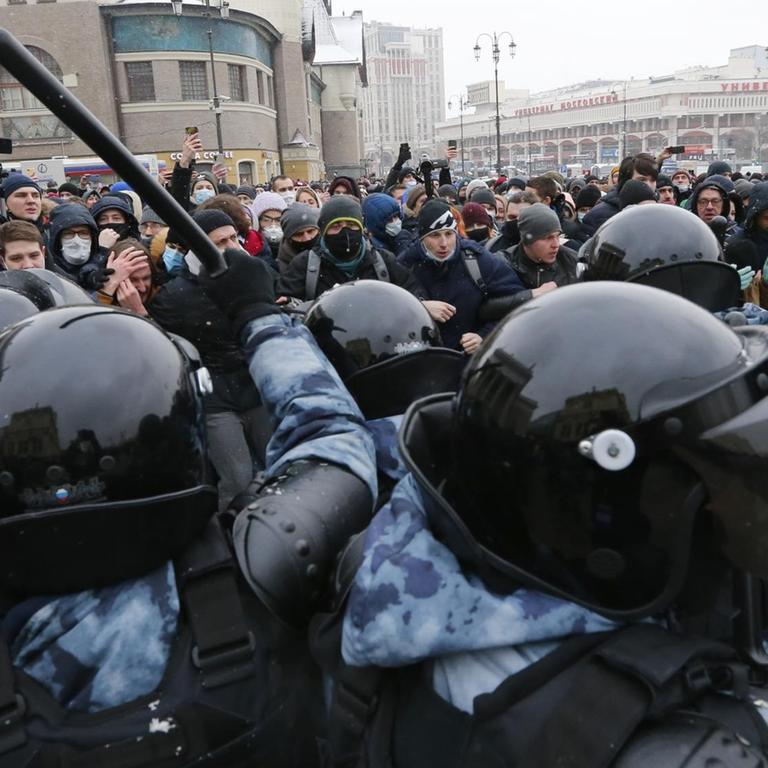 Polizisten mit Helmen und Schutzkleidung stehen einer Gruppe von Demonstranten gegenüber, ein Schlagstock ist hoch erhoben