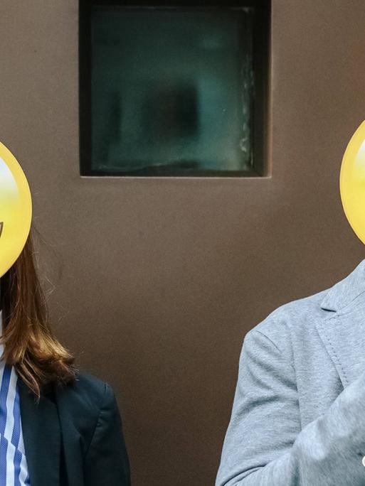 Eine Frau und ein Mann verdecken ihre Gesicher mit Emoji-Masken