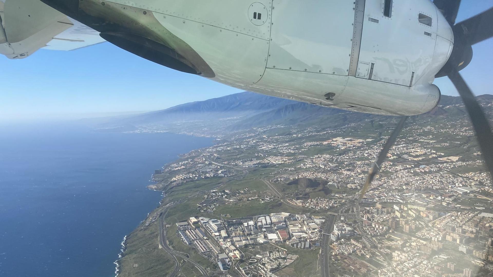 Eine Insel im Meer weit unten schaut unter einem Flugzeugflügel hervor.