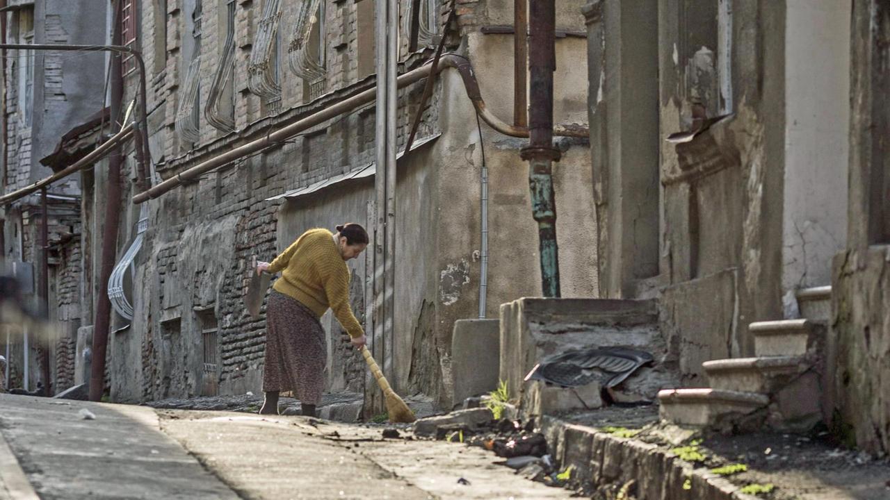 Ein Frau fegt eine Strasse in Tiflis.