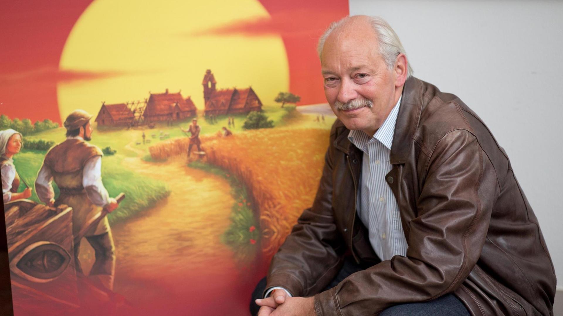 Klaus Teuber sitzt vor dem Bild seines Spiels "Die Siedler von Catan" Klaus Teuber sitzt vor dem Bild seines Spiels "Die Siedler von Catan"