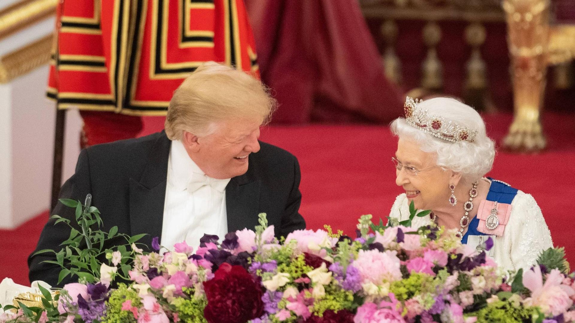 Donald Trump sitzt lachend beim Staatsbankett neben der britischen Königin. Auch die Queen lächelt.