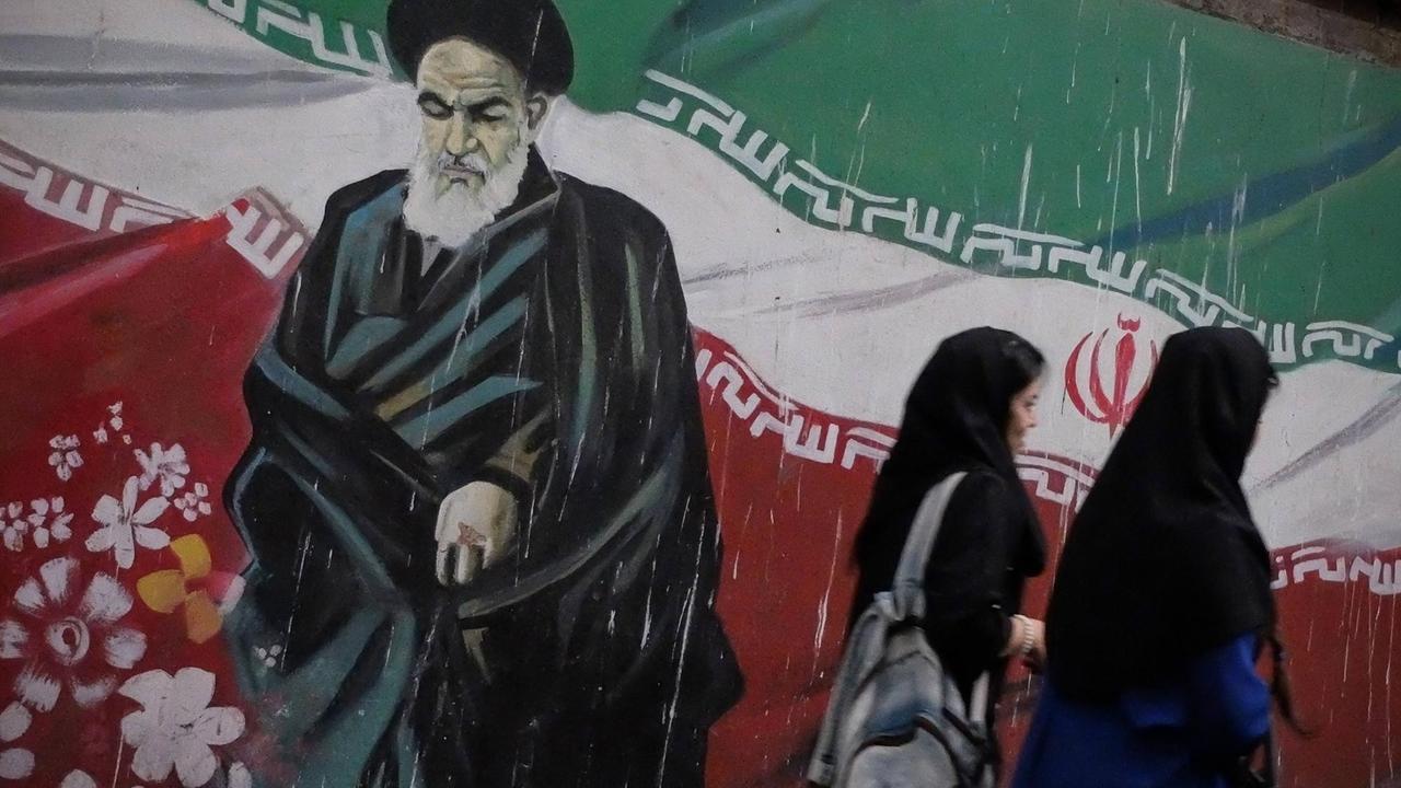 Zwei iranische Frauen vor einem Wandgemälde, das den Gründer der Islamischen Republik Iran, Ayatollah Ruhollah Khomeini, zeigt