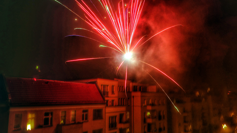 Ein rotes Feuerwerk schwebt im Dunkeln über einem Häuserdach. 