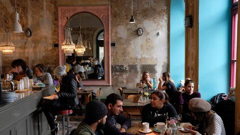 Menschen sitzen an Tischen vor den rustikalen Wänden eines Cafés