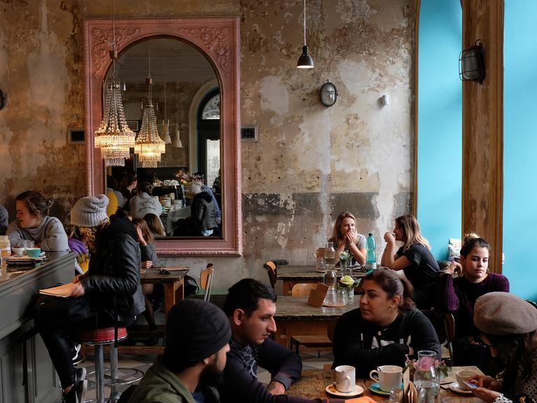 Menschen sitzen an Tischen vor den rustikalen Wänden eines Cafés