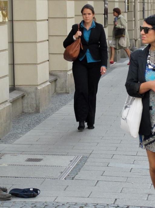 Eine Frau mit Sonnenbrille läuft vorbei an einem Bettler in der Brienner Straße in der Münchner Innenstadt.