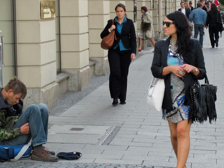 Eine Frau mit Sonnenbrille läuft vorbei an einem Bettler in der Brienner Straße in der Münchner Innenstadt.