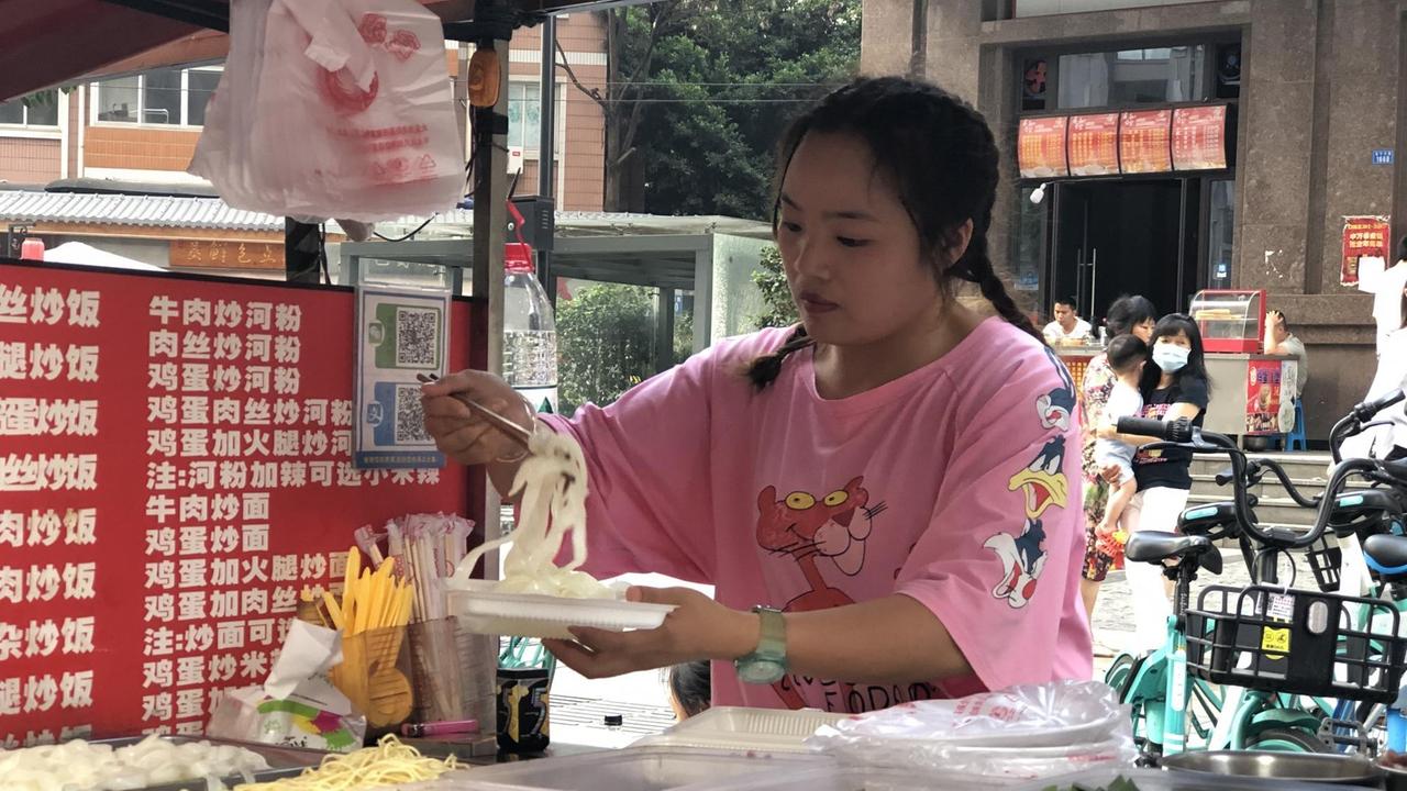 Eine junge Frau mit rosa T-Shirt bereitet auf einem Pappteller Essen zu.