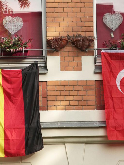 Eine rote, türkische Fahne mit dem Halbmond und dem Stern hängt während der Fußball-EM 2016 in Berlin an einem Haus neben der deutschen Flagge in Schwarz-Rot-Gold.