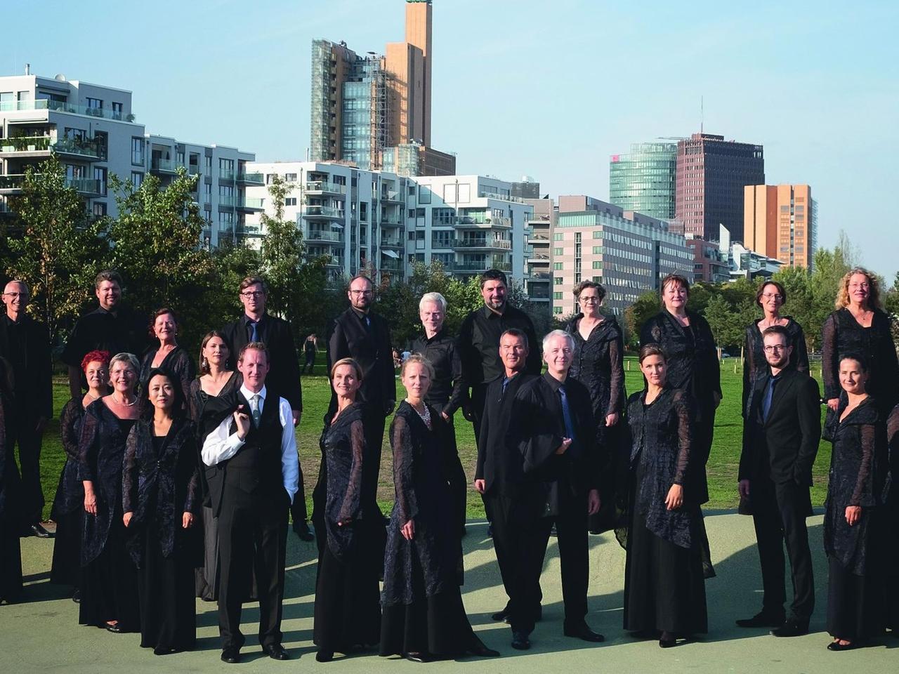 RIAS Kammerchor steht mit seinem Leiter vor der architektonischen Kulisse des Potsdamer Platzes in Berlin.