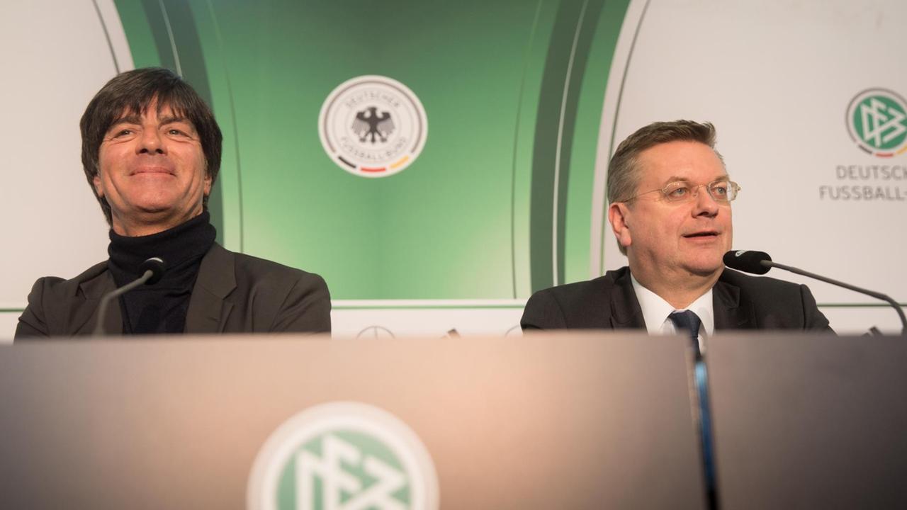 Bundestrainer Joachim Löw (l) und DFB-Präsident Reinhard Grindel (r) sitzen vor einer grün-weißen Wand mit den Logos des DFB und der deutschen Fußball-Nationalmannschaft. Löw lächelt zufrieden, Grindel redet.