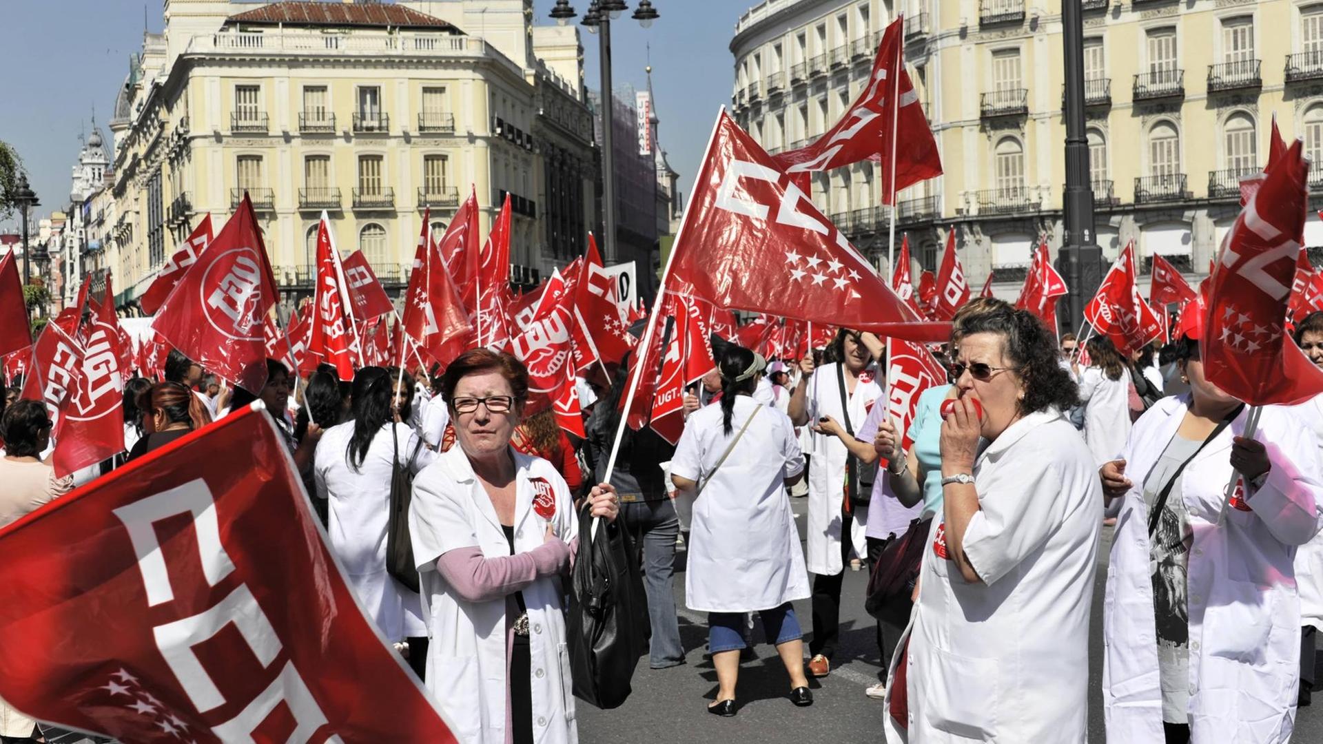 Frauen in weißen Kitteln mit roten Protestfahnen