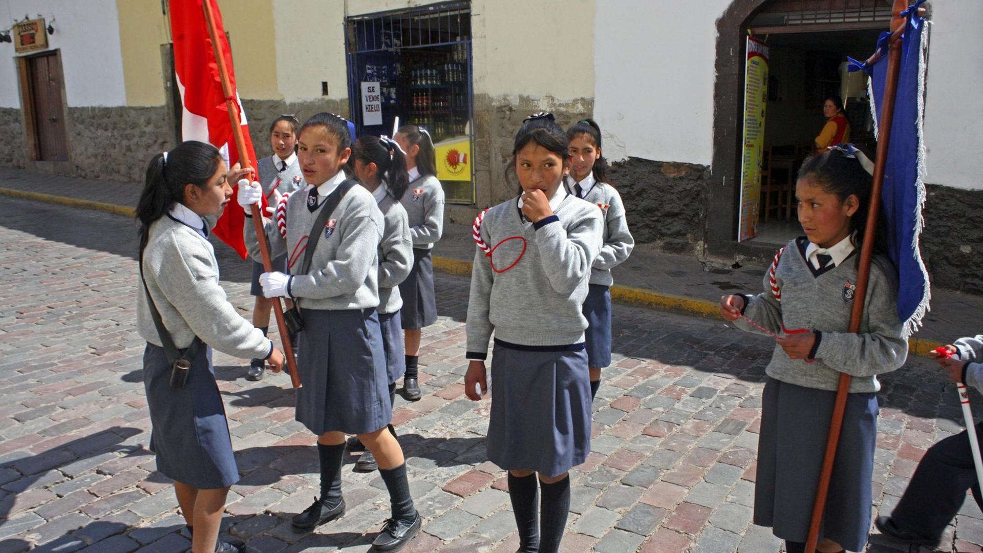 Uniformierte Schulmädchen mit peruanischer Flagge im peruanischen Cusco