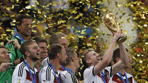 Die Nationalspieler stehen in einem Regen aus goldenen Papierschnipseln und halten den WM-Pokal in die Luft.